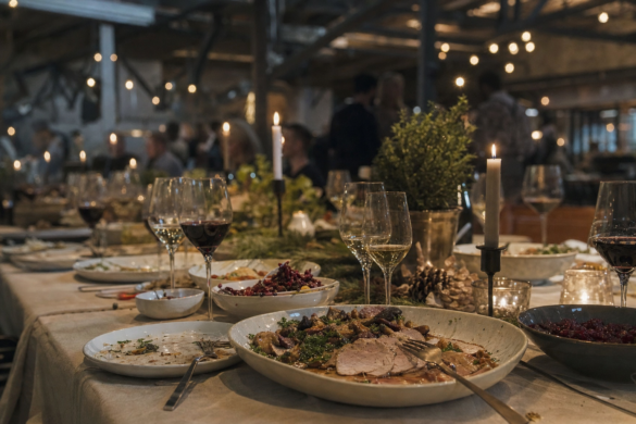 Langt julefrokostbord dækket op til firmafest i lokale med rå industrielle detaljer