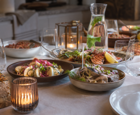 Buffetbord dækket op til julefrokost med hvid dug, glas og karafler i varmt lampelys
