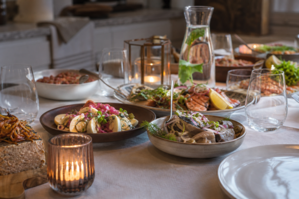 Buffetbord dækket op til julefrokost med hvid dug, glas og karafler i varmt lampelys
