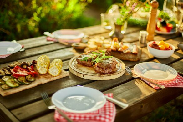 Grillede bøffer og majs på et dækket træbord til en udendørs middag